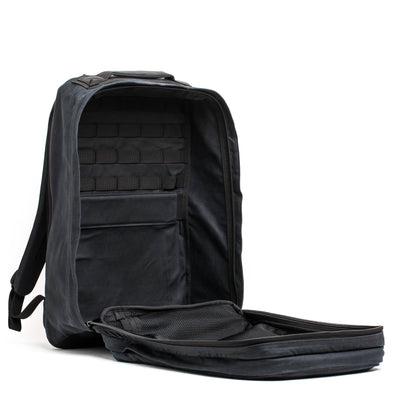 An open black GR2 - Waxed Canvas rucksack by GORUCK is displayed with its main compartment unzipped, showcasing interior pockets and a mesh section. Made from waxed duck canvas, the backpack stands upright against a white background.