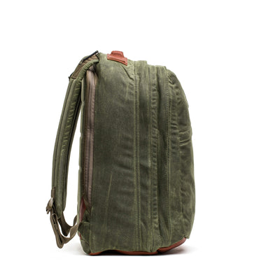 The GR2 - Waxed Canvas by GORUCK is a side view of a green canvas backpack with leather accents, crafted from durable Waxed Duck Canvas and Red Wing Leather. Featuring multiple zippers and padded shoulder straps, this bag appears sturdy and suitable for carrying various items.