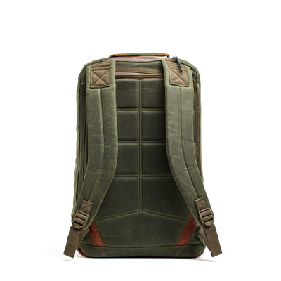 The GR2 - Waxed Canvas by GORUCK is displayed from the back, showcasing its green color with padded straps and a grid design reminiscent of a classic Heritage Retro Rucksack. It includes Red Wing Leather accents near the base and top handle, along with a zipper pocket at the top, giving it a sturdy and well-constructed appearance.