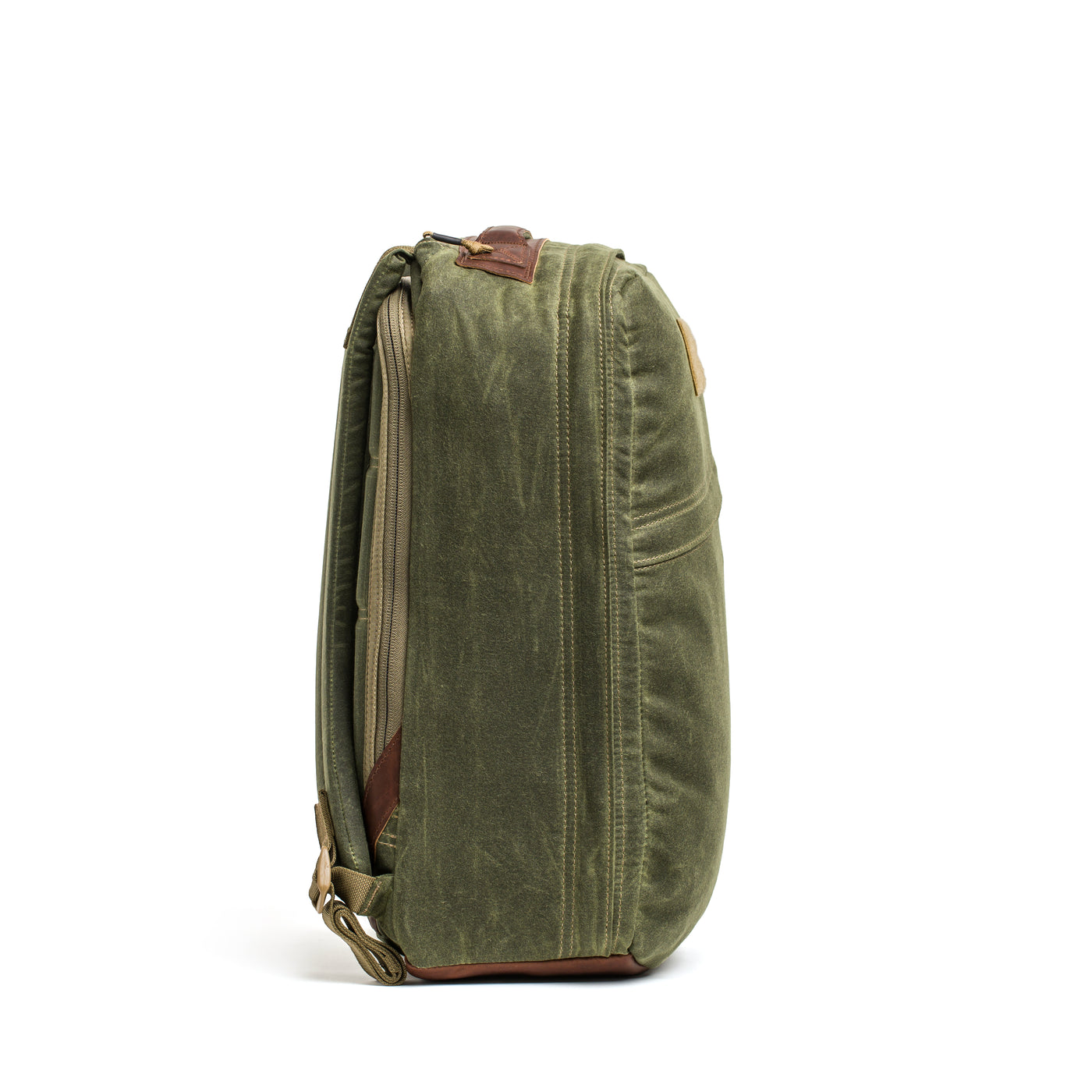 Side view of the GORUCK GR1 USA - Heritage, a green retro canvas rucksack featuring a top handle, brown leather accents, and brass hardware. This compact heritage backpack highlights visible stitching and boasts a rugged texture.