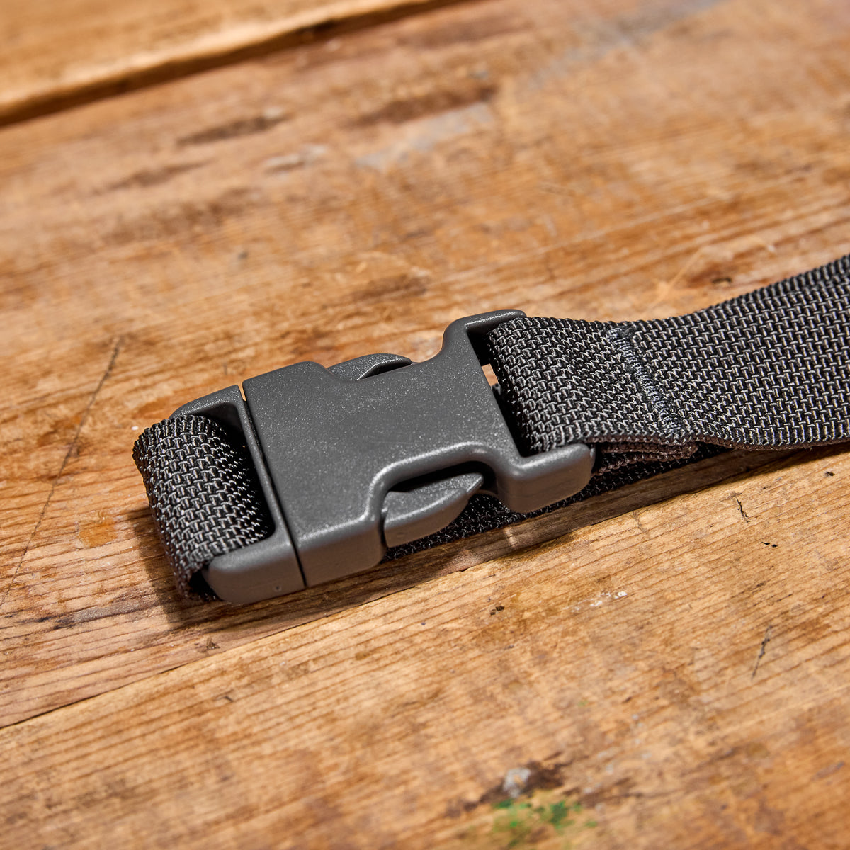 A gray plastic buckle on the black Cordura strap of a Belt Bag lies compactly on a wooden surface.