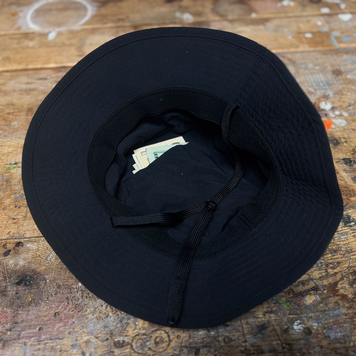 A Boonie Hat - Slick - ToughDry sits on a wooden table, lined with cash. Crafted from ToughDry® fabric, it's ideal for stashing money and offers excellent protection against the elements.