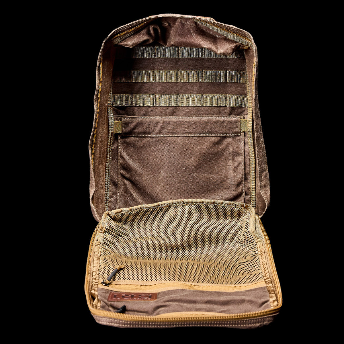 An open GR1 USA - Heritage rucksack by GORUCK, set against a black background, showcases its interior compartments featuring a mesh pocket and MOLLE straps for organization. The design is inspired by the classic GR1 style, promising both durability and efficiency.