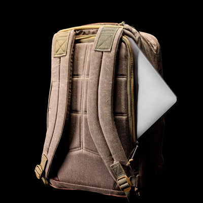 A GORUCK GR1 USA - Heritage rucksack with padded straps is set against a black background, its partially open zipper revealing a silver laptop inside.