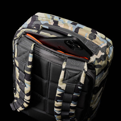 This robust GR1 USA rucksack by GORUCK showcases a camouflage design complemented by a subtle black tablet emerging from an open pocket, evoking the gear used by Special Forces against a sleek black backdrop.