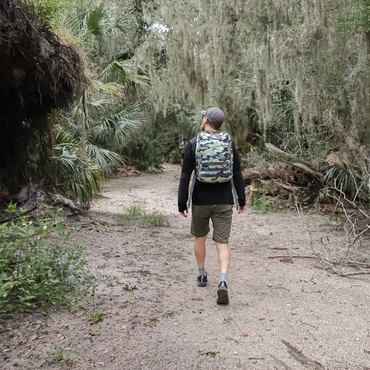 Under the canopy of moss-covered trees, a person hikes a wooded trail with the GORUCK GR1 USA - Cordura (The Original Ruck) backpack, embodying the ruggedness reminiscent of Special Forces gear.