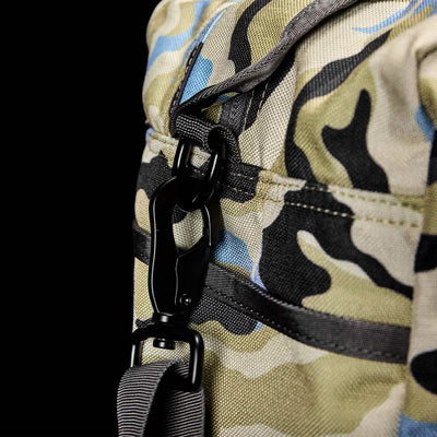 Close-up of a camouflage-patterned Kit Bag (Includes Shoulder Strap), reminiscent of an aviator’s kit bag, featuring a black metal clip securely attached to the strap.