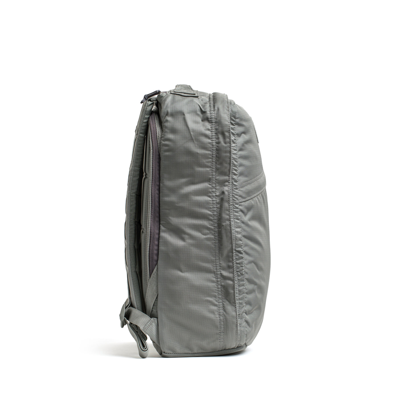 Side view of a GR1 USA - Ripstop ROBIC® backpack from GORUCK, crafted from ultra lightweight Ripstop Nylon in gray, featuring padded straps and multiple zippers on a white background.