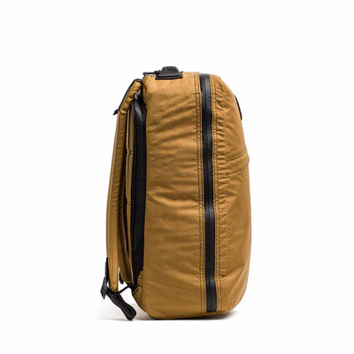 Side view of the GR1 USA - X-PAC, a tan rucksack with black zippers and straps, made from waterproof material, standing upright against a white background.