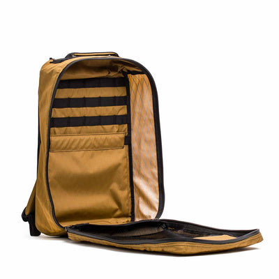 The GR1 USA - X-PAC is an open brown backpack with multiple compartments, a side zipper pocket, and AquaGuard zippers for superior water resistance.