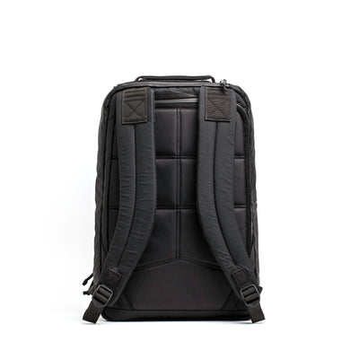 The back view of the GORUCK GR1 USA - X-PAC black rucksack features padded straps and a quilted design. Made from X-PAC material, it is waterproof. The backpack is shown upright with two adjustable shoulder straps and a top handle against a plain white background.