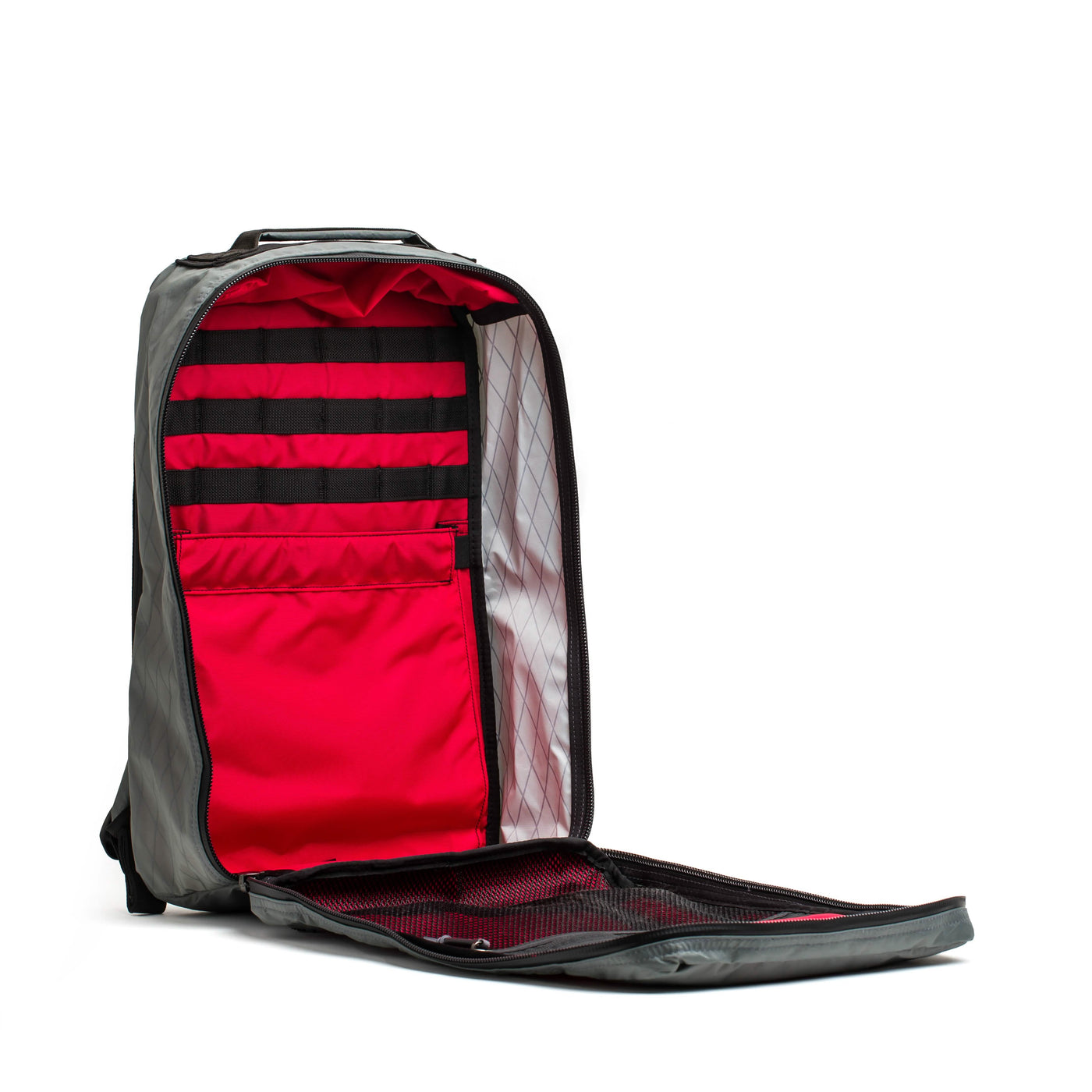 The GORUCK GR1 USA - X-PAC rucksack, featured in gray, sits open to reveal its roomy interior lined with vibrant red fabric. Inside, you'll find organized compartments and slots designed for optimal storage. The fully opened front flap showcases a mesh pocket, ensuring waterproof protection for your essentials.