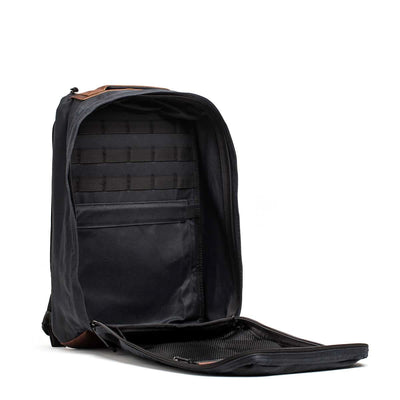 The GR1 USA - Heritage by GORUCK is made from waxed duck canvas and boasts a black exterior with an open front, highlighting its interior pockets and compartments against a white background.