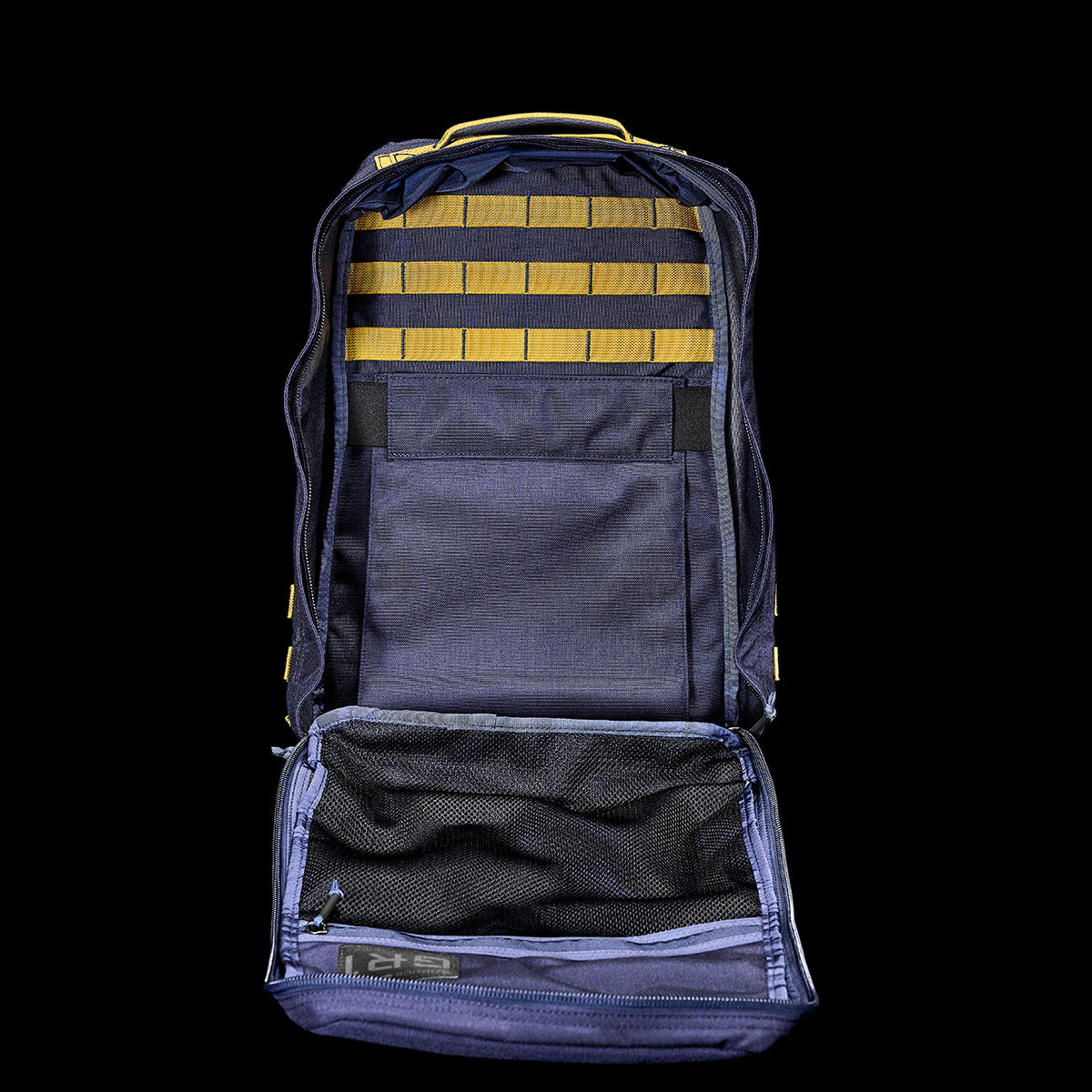 On a black background, open the blue GR1 USA Cordura by GORUCK to reveal its yellow striped interior. It showcases a bombproof laptop compartment, a mesh pocket, and a Special Forces grade build.