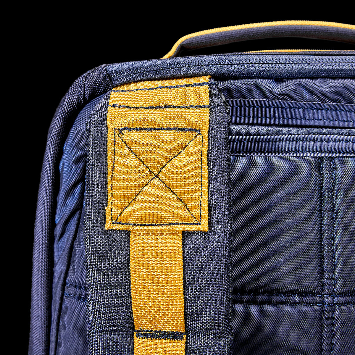 Close-up of a blue and yellow GORUCK GR1 USA - Cordura (The Original Ruck) backpack showcasing detailed stitching and texture set against a black background, highlighting its bombproof laptop compartment.