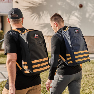 Two individuals walking outside in casual clothing, each sporting a GR1 USA - Cordura backpack featuring black and tan stripes, seem well-prepared for the next GORUCK Challenge.