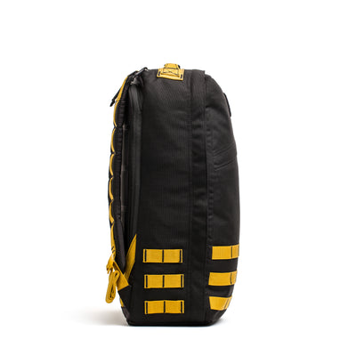 Side view of a black and yellow GR1 USA - Cordura (The Original Ruck) backpack by GORUCK, featuring multiple attachment loops on a white background. Expertly crafted in America, this model is perfectly designed for rugged use, embodying the durability preferred by Special Forces.