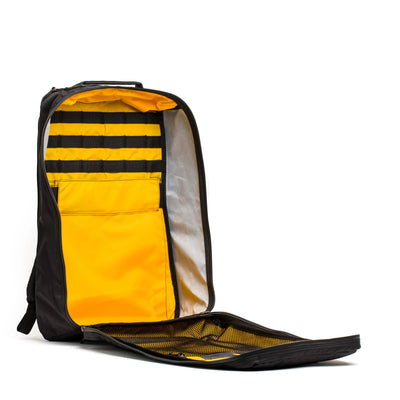 The GR1 USA - X-PAC rucksack by GORUCK is open, revealing its interior. It features multiple compartments with pockets and elastic bands for organized storage. The bright yellow lining contrasts sharply with the waterproof black exterior.