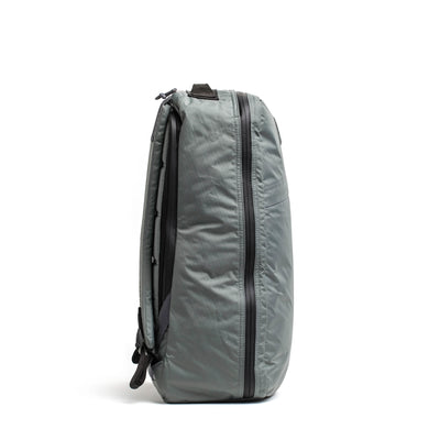 The GR1 USA - X-PAC by GORUCK is a modern and functional gray rucksack made with waterproof X-PAC fabric. Featuring a sleek design, it stands upright with a central horizontal zipper and padded shoulder straps, showcasing its minimalist aesthetic and smooth texture.