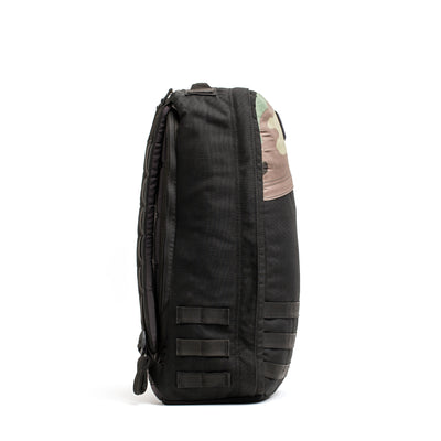 Side view of the GORUCK GR1 Birdwell backpack, highlighted by a camo-patterned top section made with SurfNyl™️. This black backpack features multiple compartments and attachment loops, perfect for outdoor or tactical activities. It proudly displays American craftsmanship against a plain white backdrop.