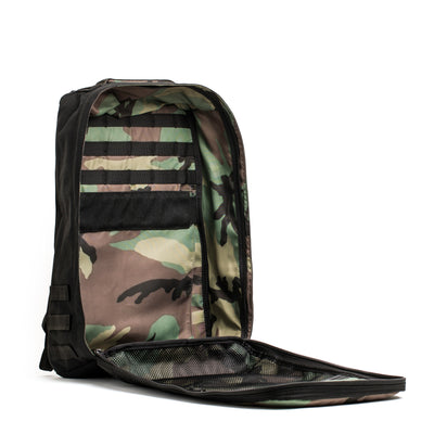 The GR1 Birdwell by GORUCK proudly displays its American craftsmanship with an open camouflage design, highlighting its interior pockets and mesh sections. The front flap lies flat to reveal the storage compartments and a bombproof laptop compartment, all made from water-repellent SurfNyl for added durability.