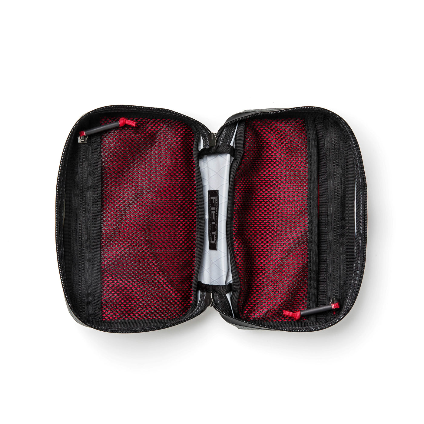 An open GORUCK GR1 Field Pocket USA - X-PAC in black with a red interior and black mesh pockets on either side. In the center, a small, folded white item with text is secured by straps. The two red zipper pulls suggest its potential as an essential travel accessory.