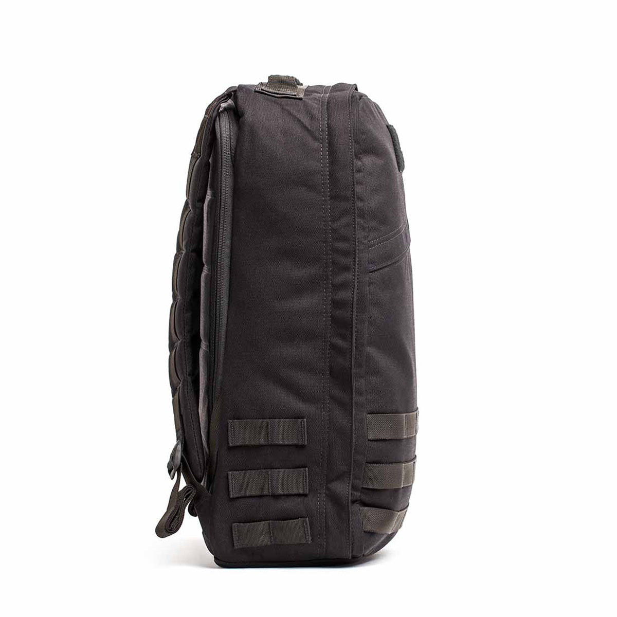 Side view of the GR1 USA Throwback backpack in dark gray, made from 1680 Ballistic Nylon. It features horizontal straps, a padded shoulder strap, and a bombproof laptop compartment for protection.