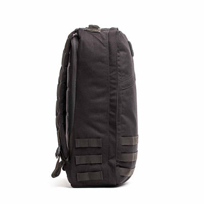 Side view of the GR1 USA Throwback backpack in dark gray, made from 1680 Ballistic Nylon. It features horizontal straps, a padded shoulder strap, and a bombproof laptop compartment for protection.