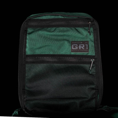 Dark green and black durable rucksack named "GR1 USA - Cordura" from GORUCK, showcasing a "GR1" patch and zippers on the front, inspired by Special Forces design.