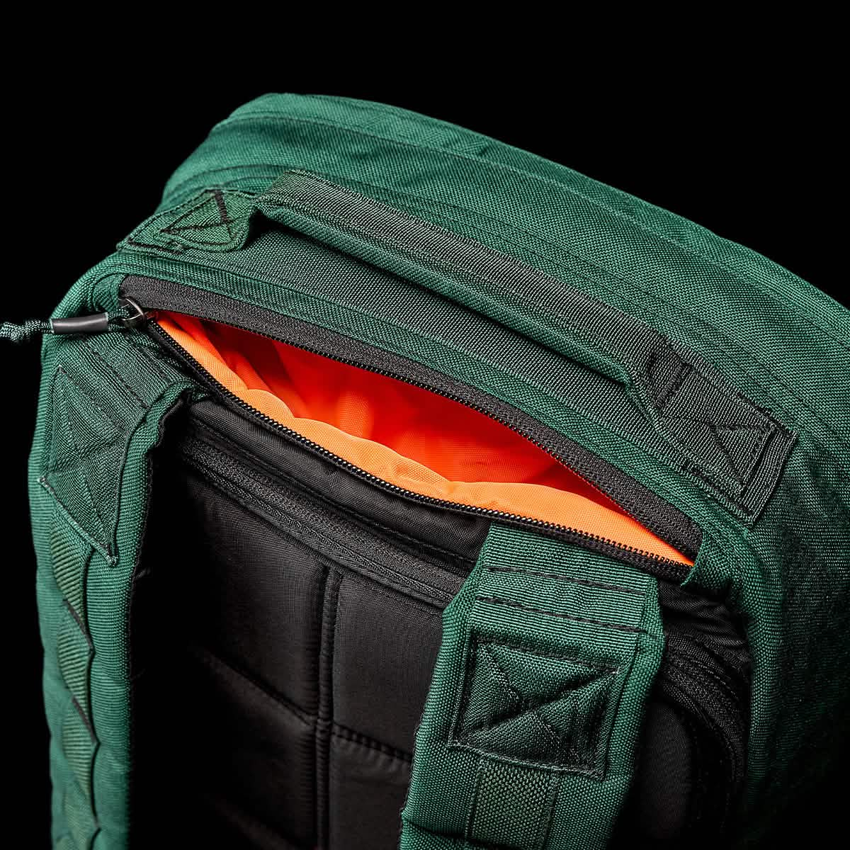 The GR1 USA - Cordura (The Original Ruck) by GORUCK is a durable rucksack that features a green exterior and a vibrant orange interior. Its partially unzipped design reveals robust black padded straps, akin to those used by Special Forces, against a sleek black background.