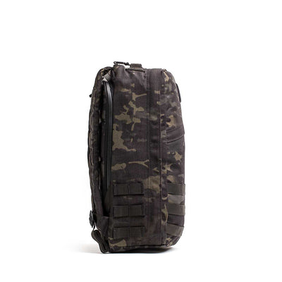 Side view of the GR1 USA - Cordura, a black tactical backpack made with Special Forces-grade materials. It has multiple straps and compartments, perfect for enduring the GORUCK Challenge.