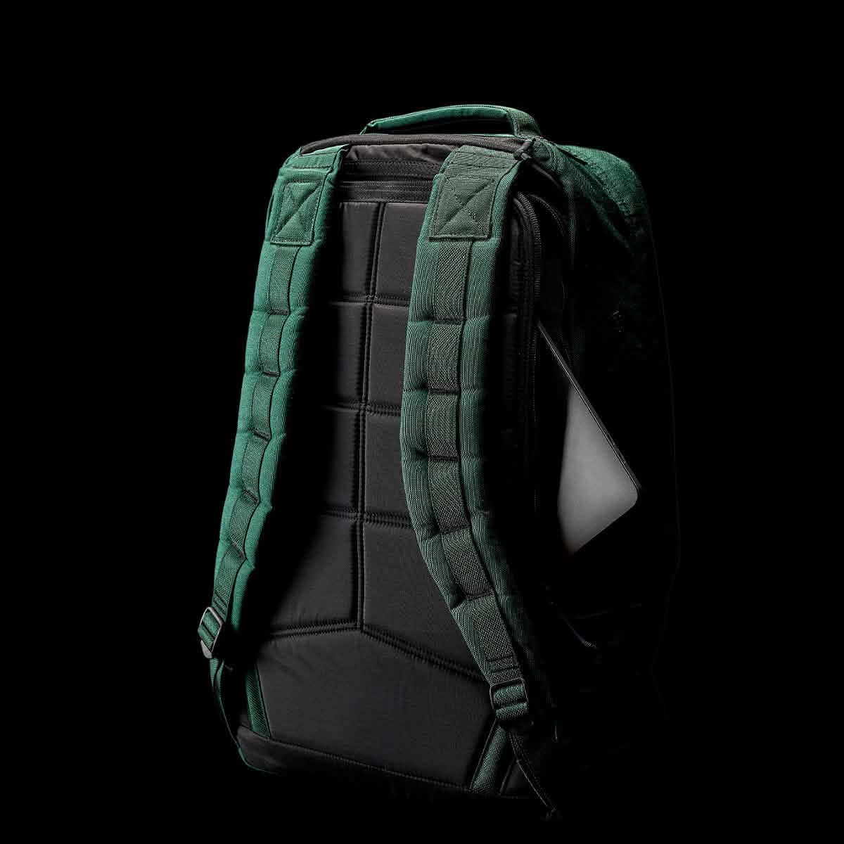 The GR1 USA - Cordura (The Original Ruck) backpack by GORUCK, in green and black with padded straps and a partially visible white laptop inside, is designed for endurance like a GORUCK Challenge, set against a sleek black background.