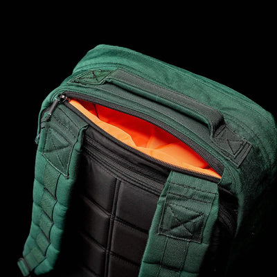 The GR1 USA - Cordura (The Original Ruck) by GORUCK is displayed on a sleek black background, featuring a green design with black padded straps and an orange-lined zip pocket, reminiscent of the rugged backpacks used in GORUCK Challenges.