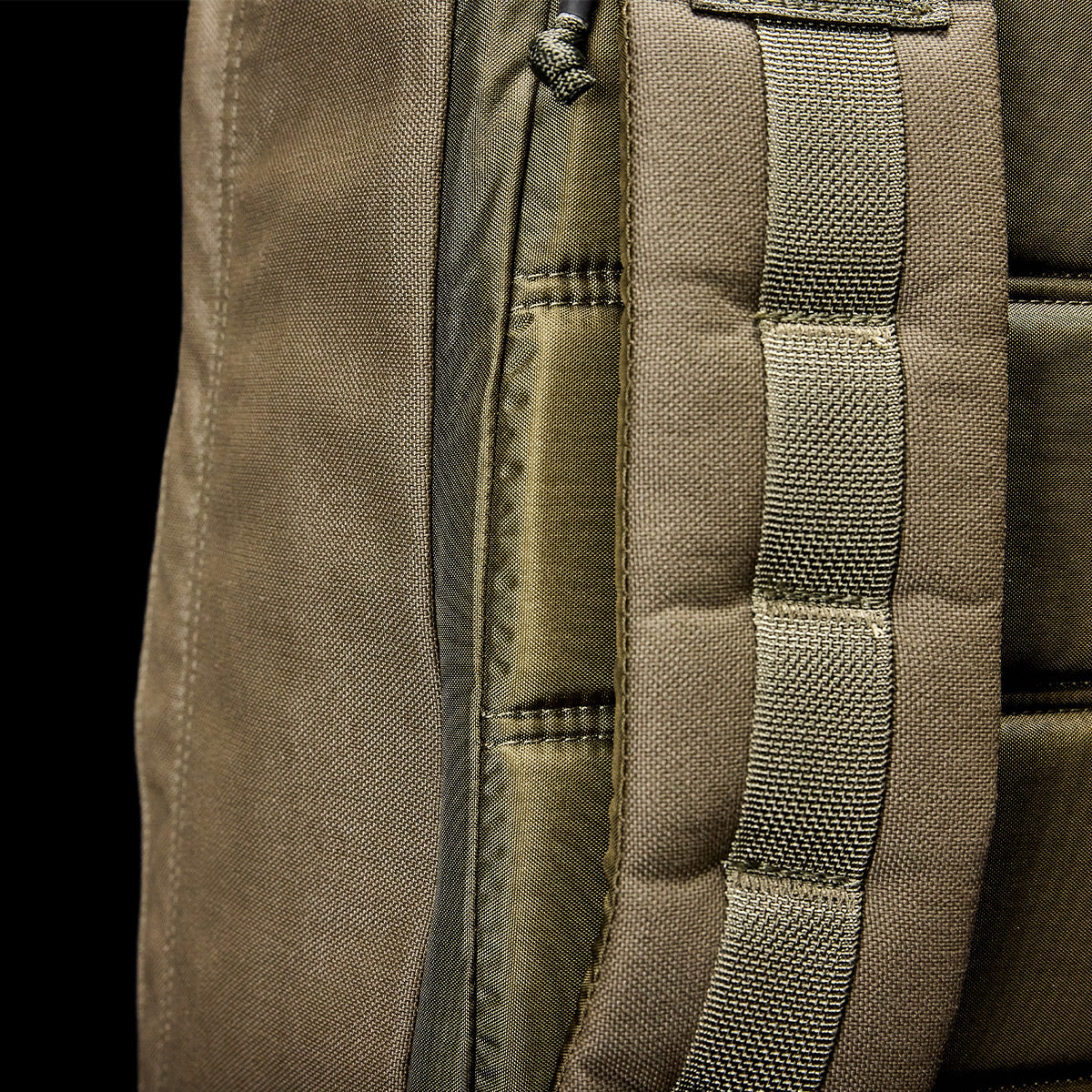 Close-up of the GR1 USA - Cordura (The Original Ruck), a khaki backpack made with Special Forces-grade materials, featuring intricate stitching and a woven strap, set against a black background.