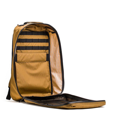 The GR1 USA - X-PAC is a tan rucksack with black accents, made from durable X-PAC material. It has internal pockets and compartments, an invitingly unzipped zipper, and combines style with practicality while being waterproof. Photographed isolated on white.