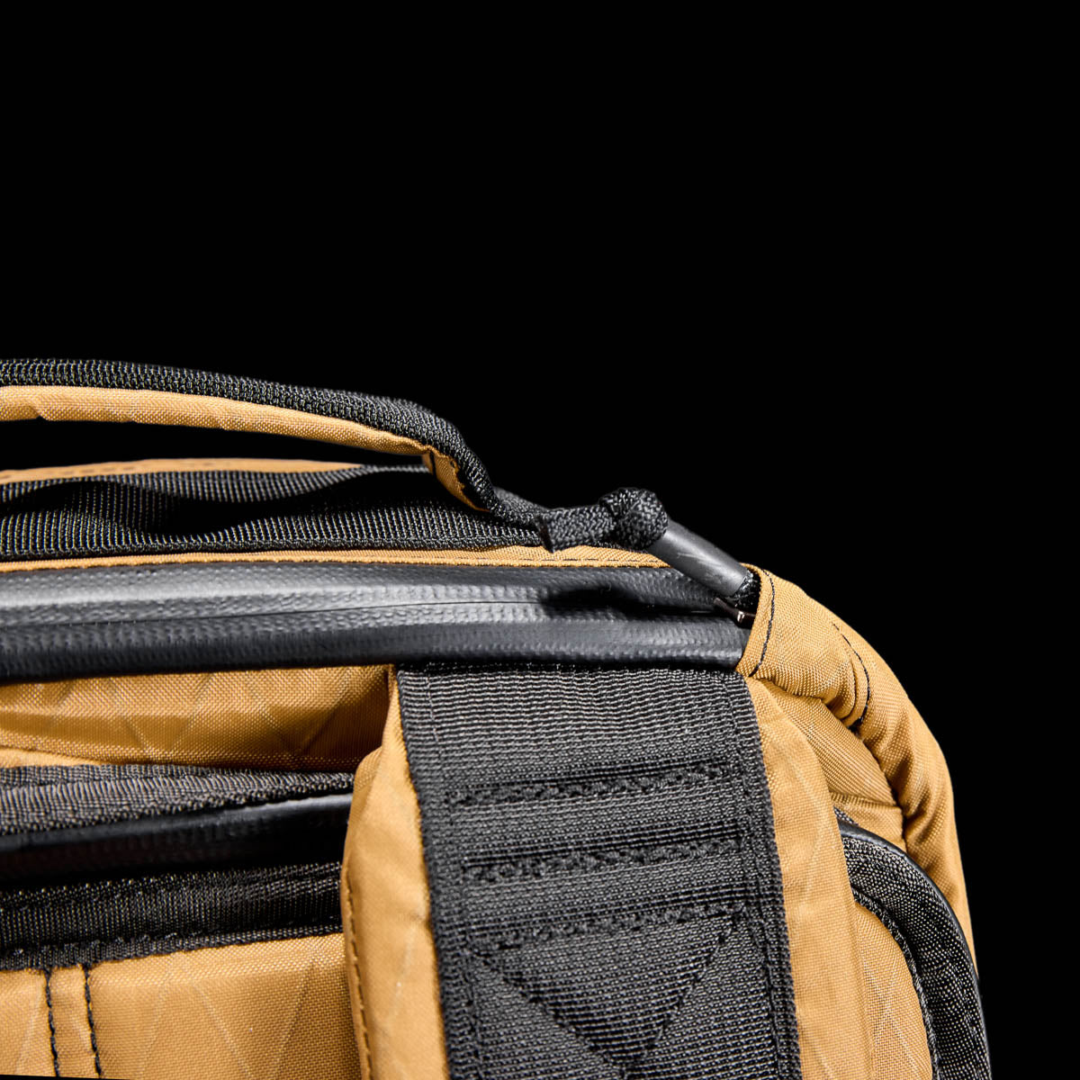 Close-up of the GR1 USA - X-PAC rucksack in tan and black, highlighting the strap and top zipper against a black backdrop.