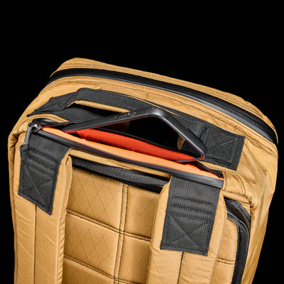 The GR1 USA - X-PAC is a tan quilted backpack with AquaGuard zippers and adjustable black straps. It features an open top compartment with a striking red interior, ensuring both security and style for your belongings.