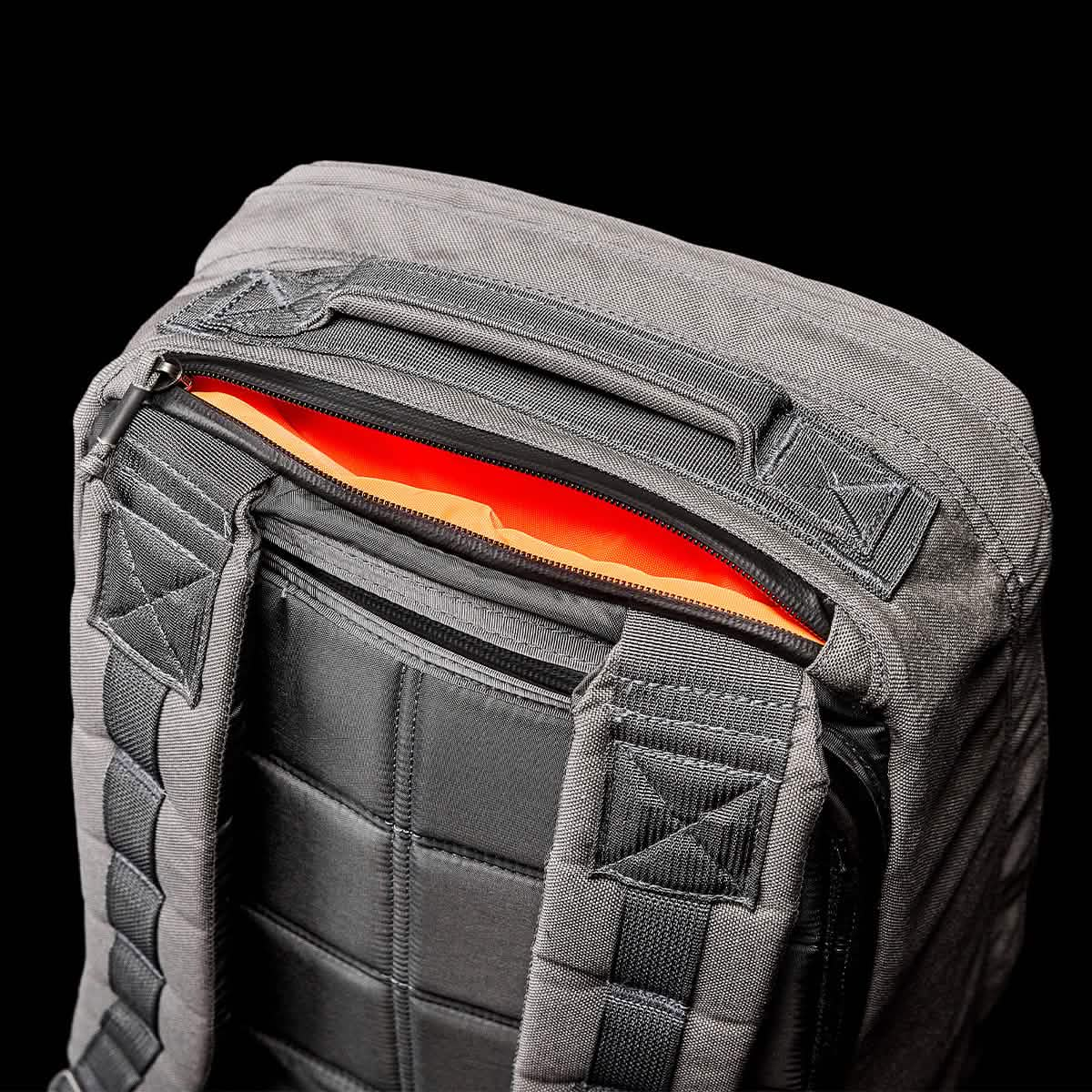 The GORUCK GR1 USA - Cordura (The Original Ruck) is a gray backpack inspired by Special Forces gear, featuring black padded straps and an orange interior, all highlighted against a sleek black background. It is precisely crafted in American manufacturing, combining durability with style.