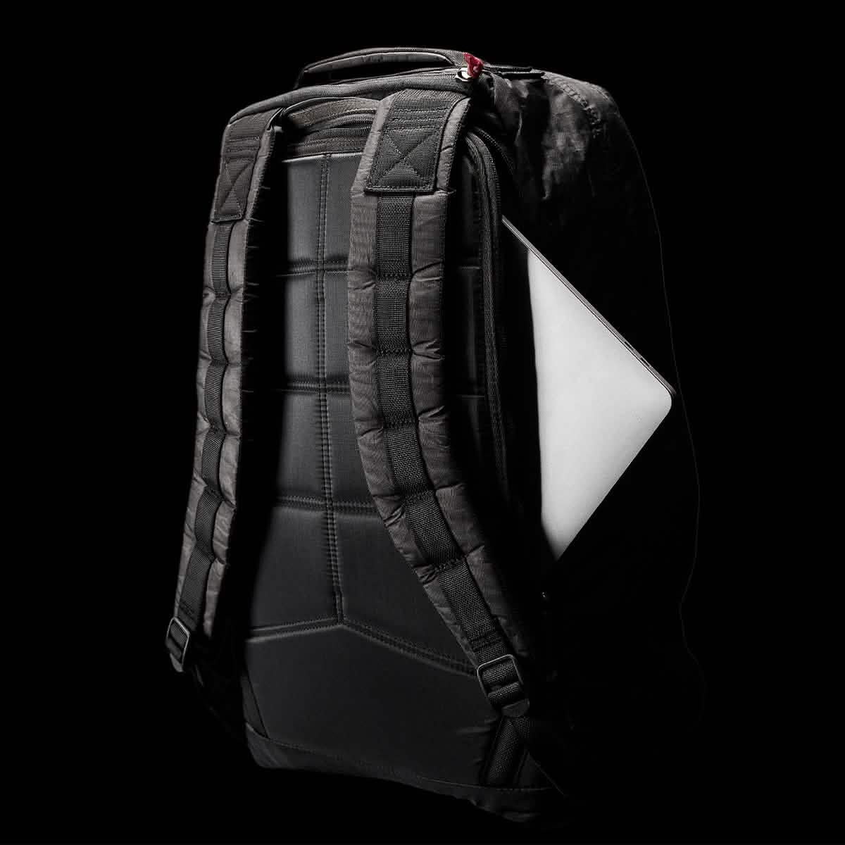 A black GR1 USA - Dyneema rucksack by GORUCK set against a dark background, highlighting its padded shoulder straps and sleek design. A white laptop peeks out from the side pocket, accentuating the impressive storage capability of this Dyneema® rucksack.