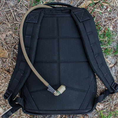 The GR1 USA Throwback, made from 1680 ballistic nylon, boasts a bombproof laptop compartment, padded straps, and a tan hydration tube. It's rugged and adventure-ready as it sits on the leaf-strewn ground.