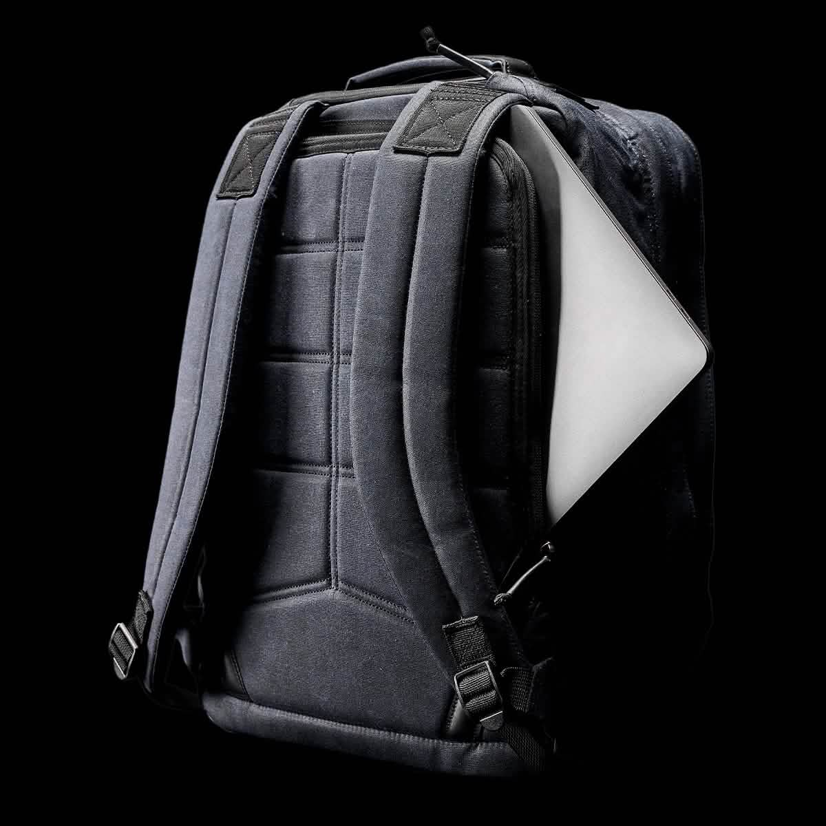 The GR2 - Waxed Canvas by GORUCK, featuring padded straps and a quilted back, is displayed against a black background. A laptop can be seen partially emerging from the side of the backpack.