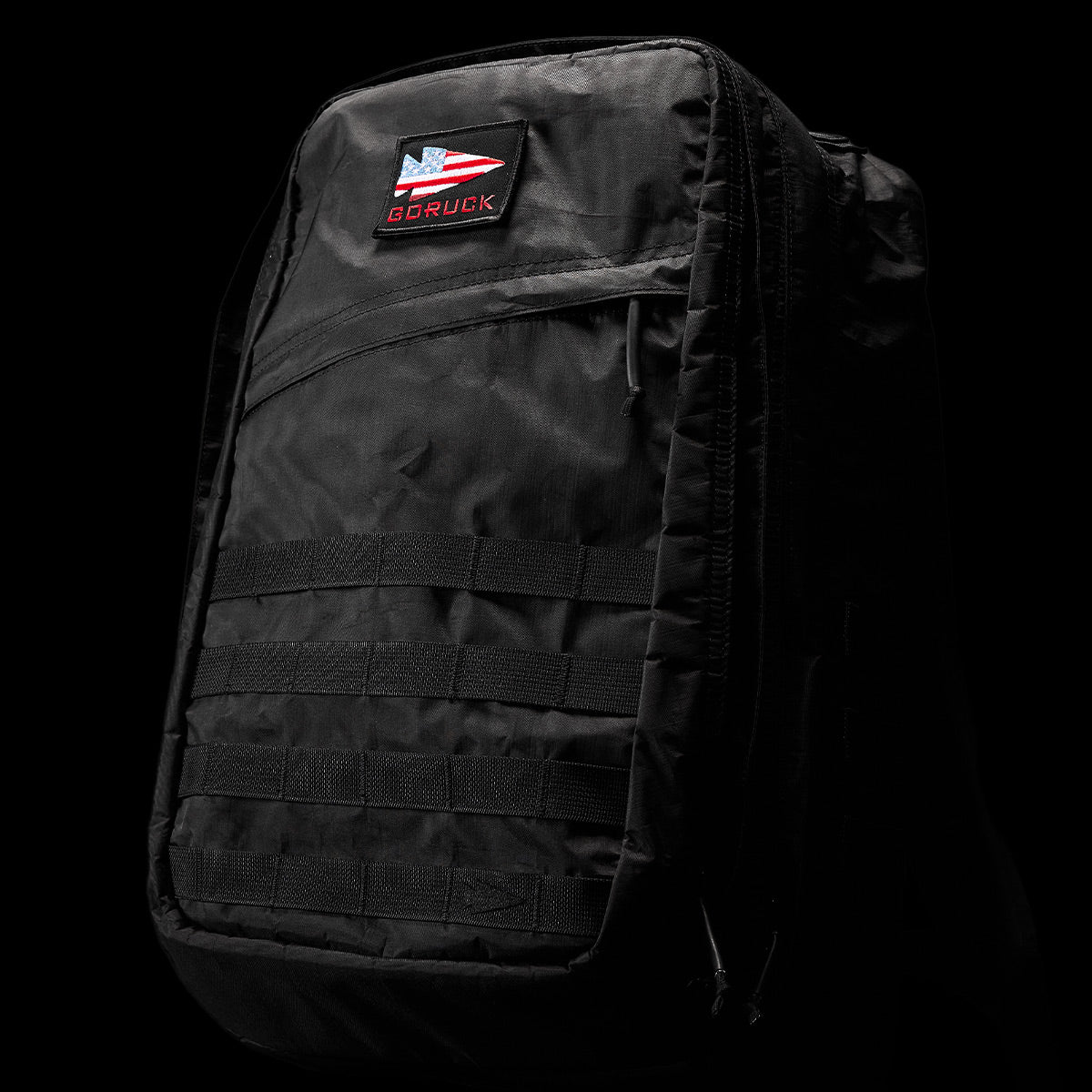 The GR2 - Dyneema backpack by GORUCK features a rugged design crafted from abrasion-resistant materials, with a striking red and white logo patch near the top. This model includes multiple compartments and a grid of horizontal straps on the front, all set against its sleek black background.