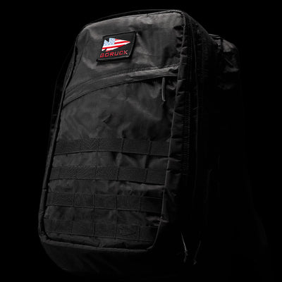 The GR2 - Dyneema backpack by GORUCK features a rugged design crafted from abrasion-resistant materials, with a striking red and white logo patch near the top. This model includes multiple compartments and a grid of horizontal straps on the front, all set against its sleek black background.