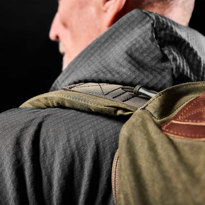 Close-up of a person wearing a jacket with a hood, carrying the GORUCK GR2 Waxed Canvas rucksack. The image is focused on the shoulder area, emphasizing the backpack strap and jacket texture against a dark background.