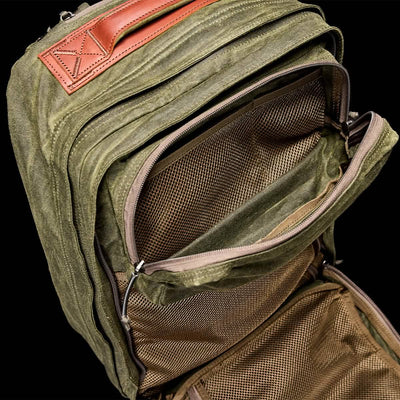 The olive green GR2 - Waxed Canvas backpack by GORUCK features a Heritage Retro Rucksack style, accented with premium Red Wing Leather and multiple compartments. The interior includes mesh pockets, and the partially undone zippers reveal its impressive storage capacity against a black background.