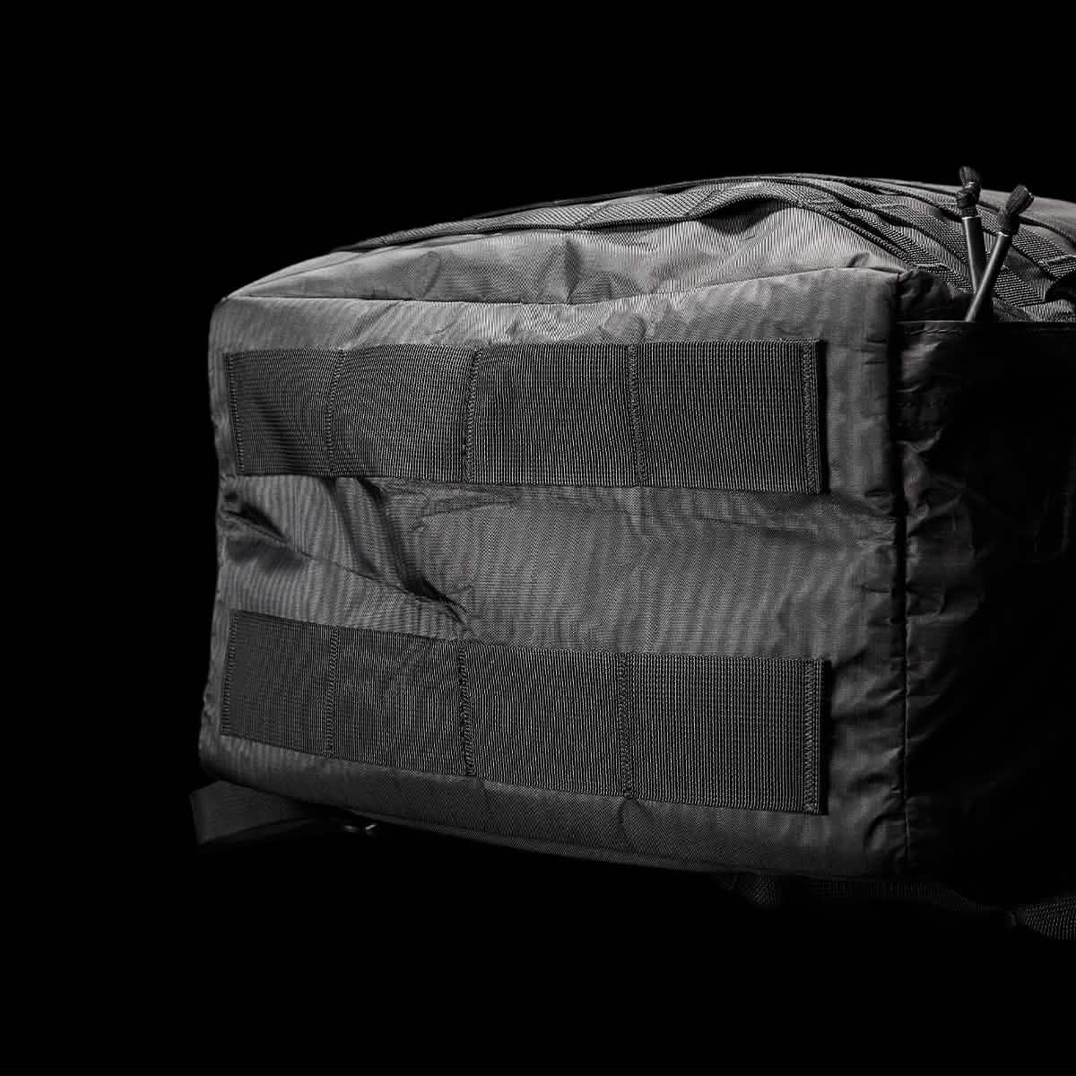 Close-up of the GR3 - Dyneema, a black tactical carry-on backpack by GORUCK, set against a dark background. The focus is on its sturdy fabric and webbing straps made from durable Dyneema material, highlighting its rugged design and durability backed by the reassurance of GORUCK's Scars Lifetime Guarantee.