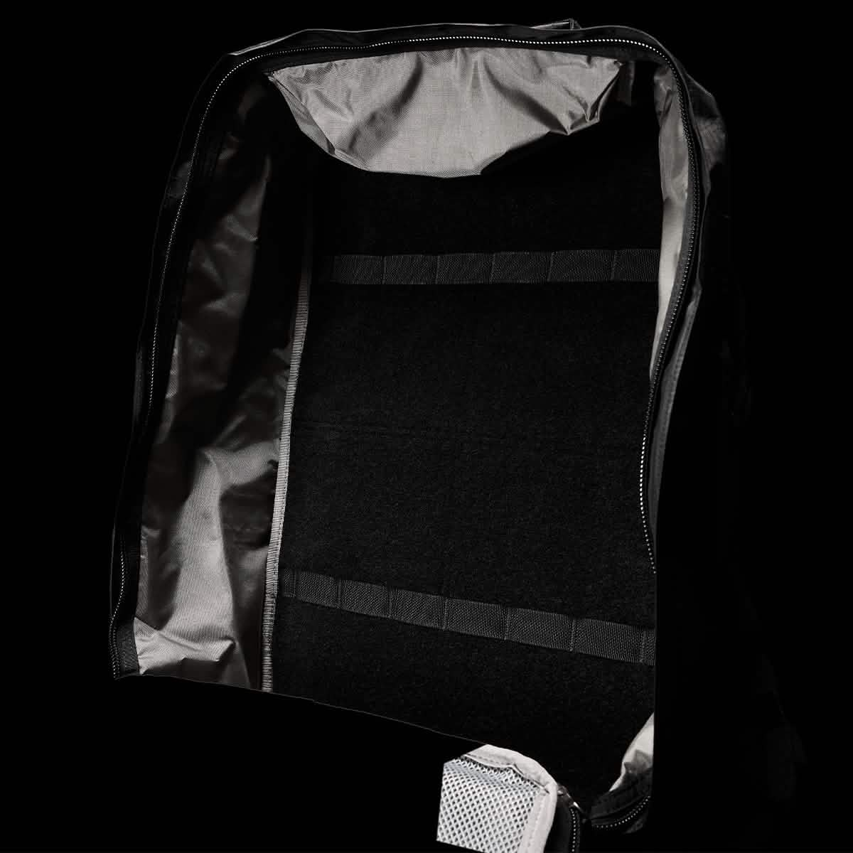 Unzip the GR3 - Dyneema, a black carry-on backpack from GORUCK, revealing its grey interior and emphasizing its multiple straps and compartments. Made from durable Dyneema material, the image showcases the spacious main compartment with its interior lining and zipper details against a dark background.