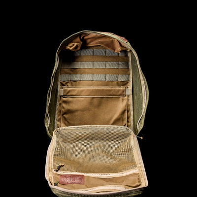 Against a black background is the open GR1 USA - Heritage rucksack in olive green by GORUCK, showcasing multiple compartments and mesh pockets. The interior highlights heritage beige and khaki fabric with organized straps for storage, blending functionality with classic style.