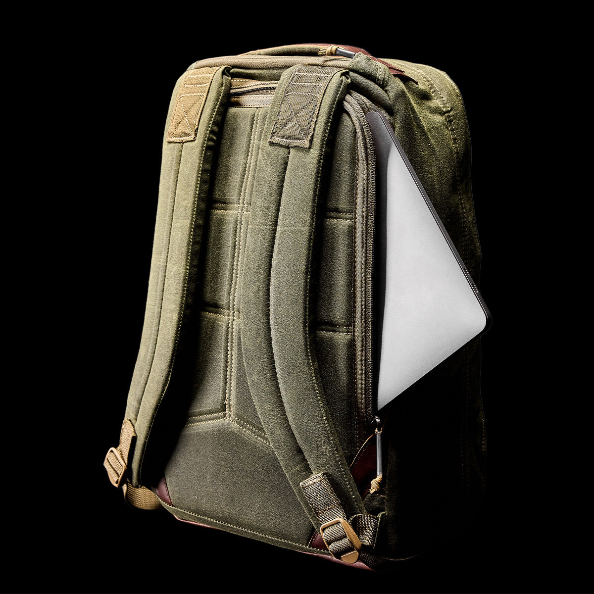 A GORUCK GR1 USA - Heritage rucksack stands upright against a black background, with a tablet partially tucked into its side pocket. The backpack features padded straps and reinforced stitching, offering both style and durability.