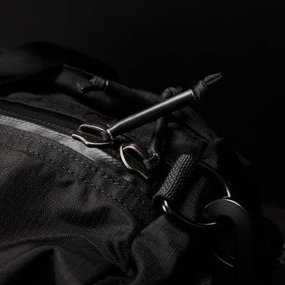 Close-up of a GORUCK Gym Bag - Ripstop ROBIC® backpack highlights the zipper and pull tags. The textured ripstop nylon with detailed stitching features metal zippers and loops. The dark background emphasizes the bag's design, suggesting a concealed shoe compartment for extra convenience.